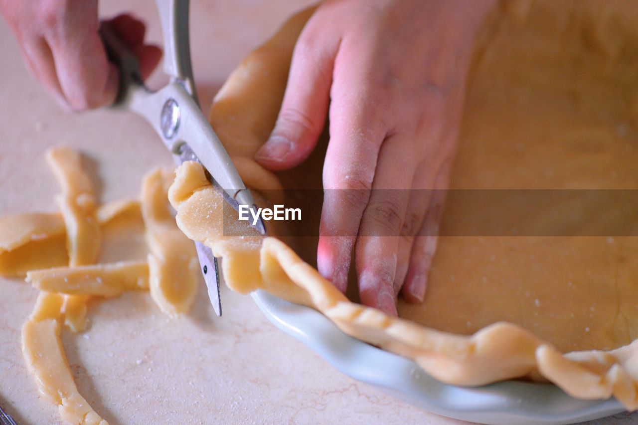 Cropped hands cutting pie dough in kitchen