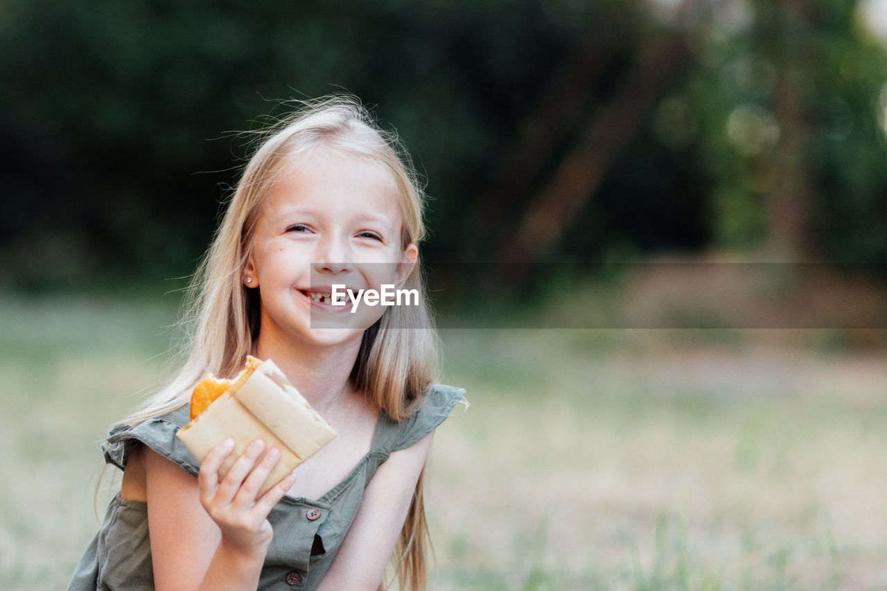 Portrait of smiling girl eating food at park