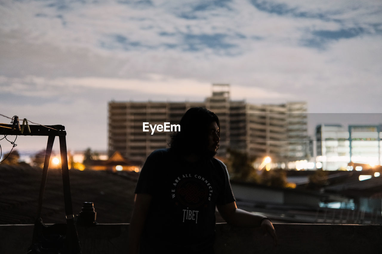 REAR VIEW OF MAN LOOKING AT CITYSCAPE AGAINST SKY