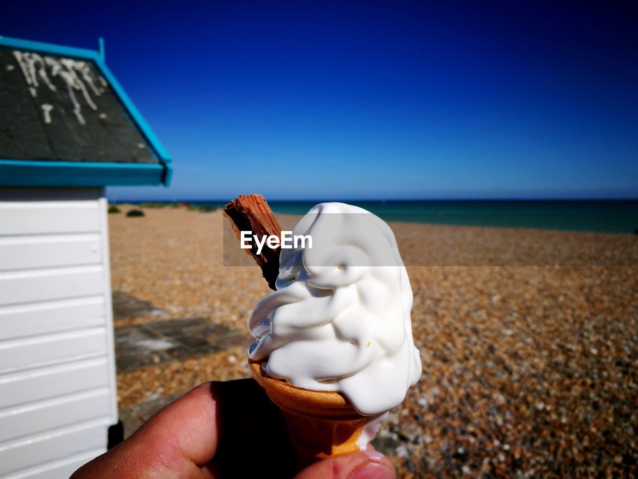 MIDSECTION OF PERSON HOLDING ICE CREAM AGAINST SEA