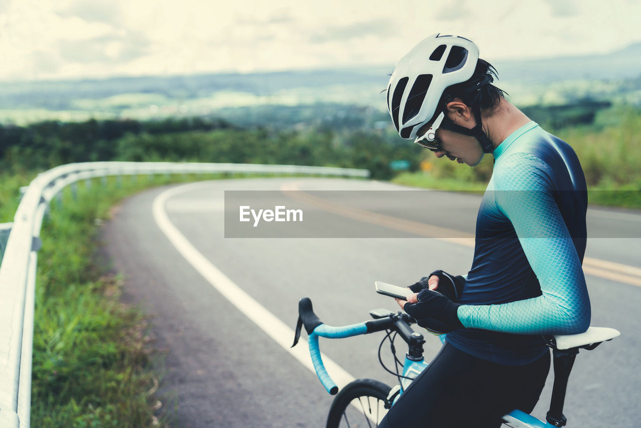 Mid adult man using phone sitting on bicycle at road