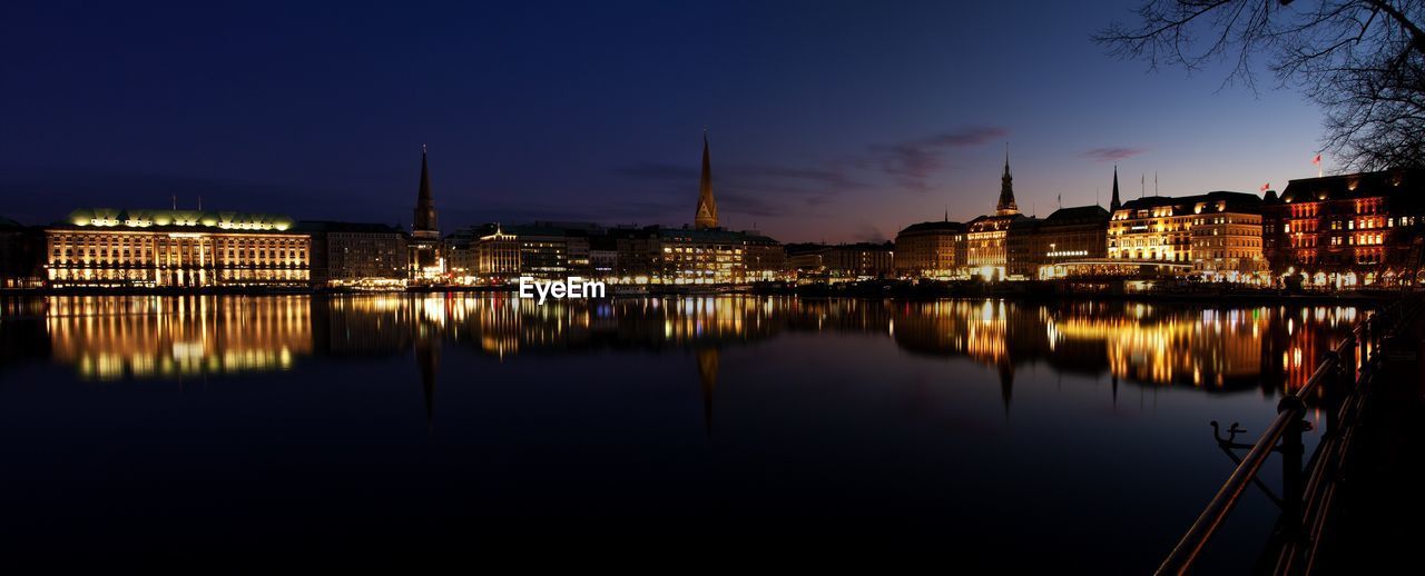 Panoramic view of buildings glowing by alster river at night