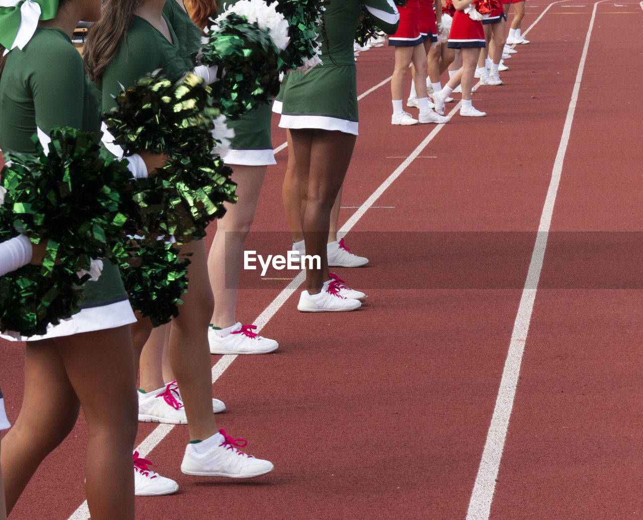 Side view of two cheerleading squads standing on sideline cheering  teams during a football game.