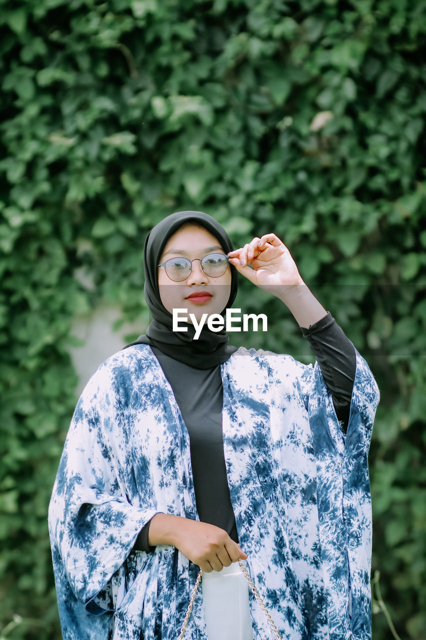 Young woman wearing sunglasses standing against plants