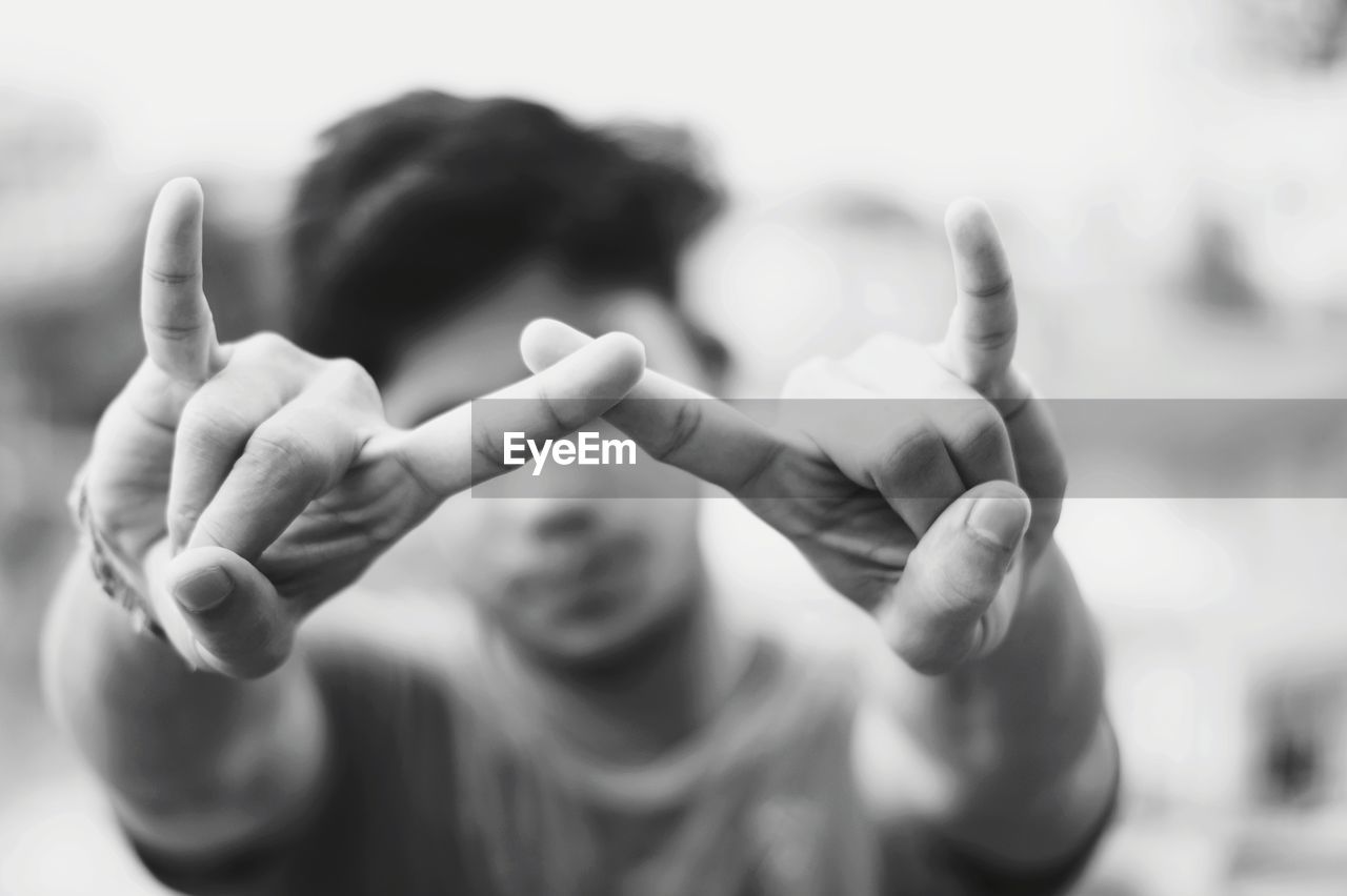 Close-up of young man gesturing horn sign while standing outdoors