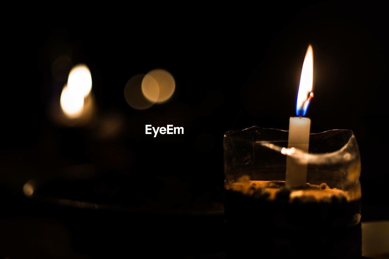 CLOSE-UP OF LIT TEA LIGHT CANDLES IN DARK ROOM