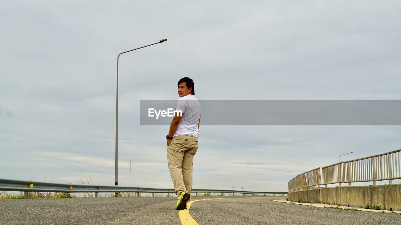 Rear view portrait of man walking on road against cloudy sky