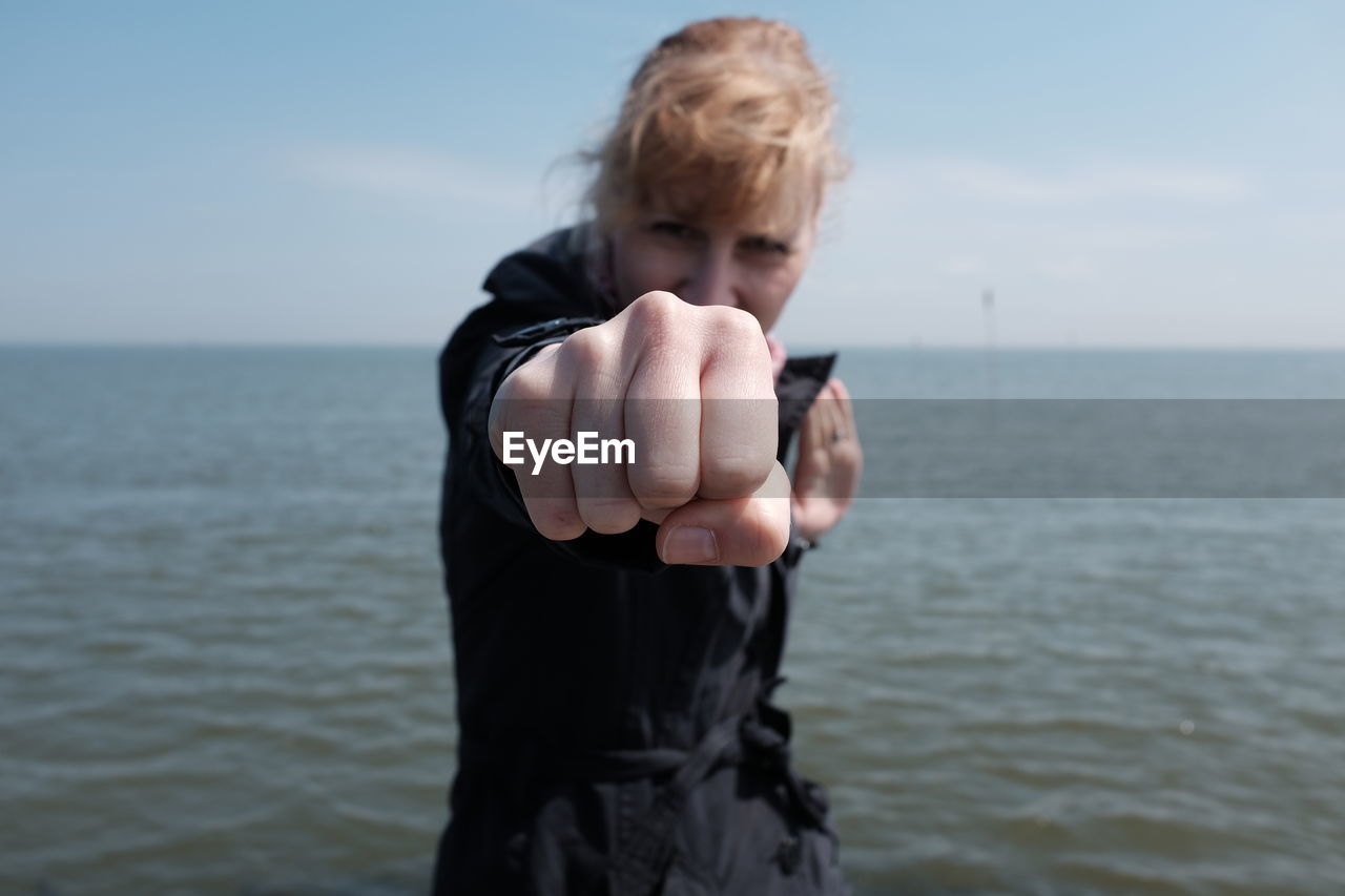 Portrait of young woman fighting stance against sea