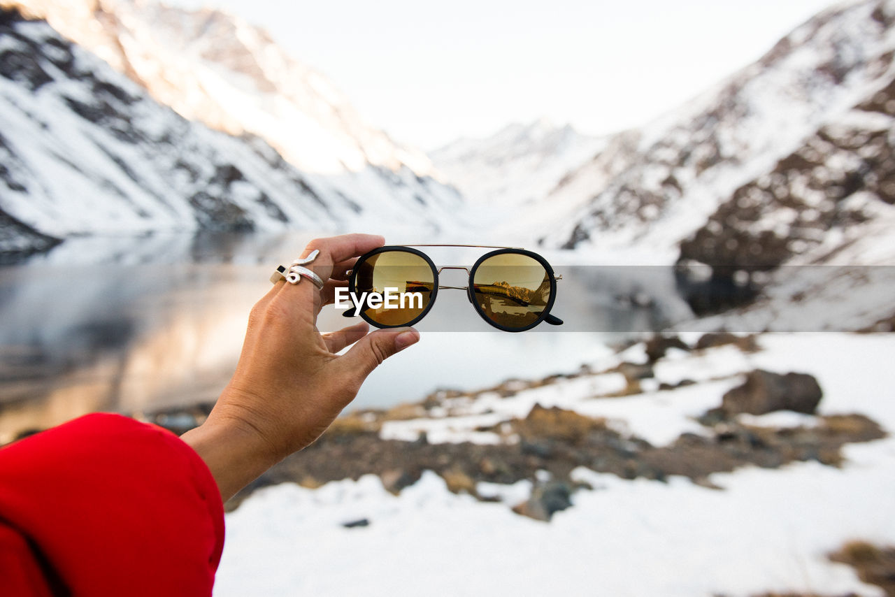 A tourist holds up a pair of stylish sunglasses in the mountains