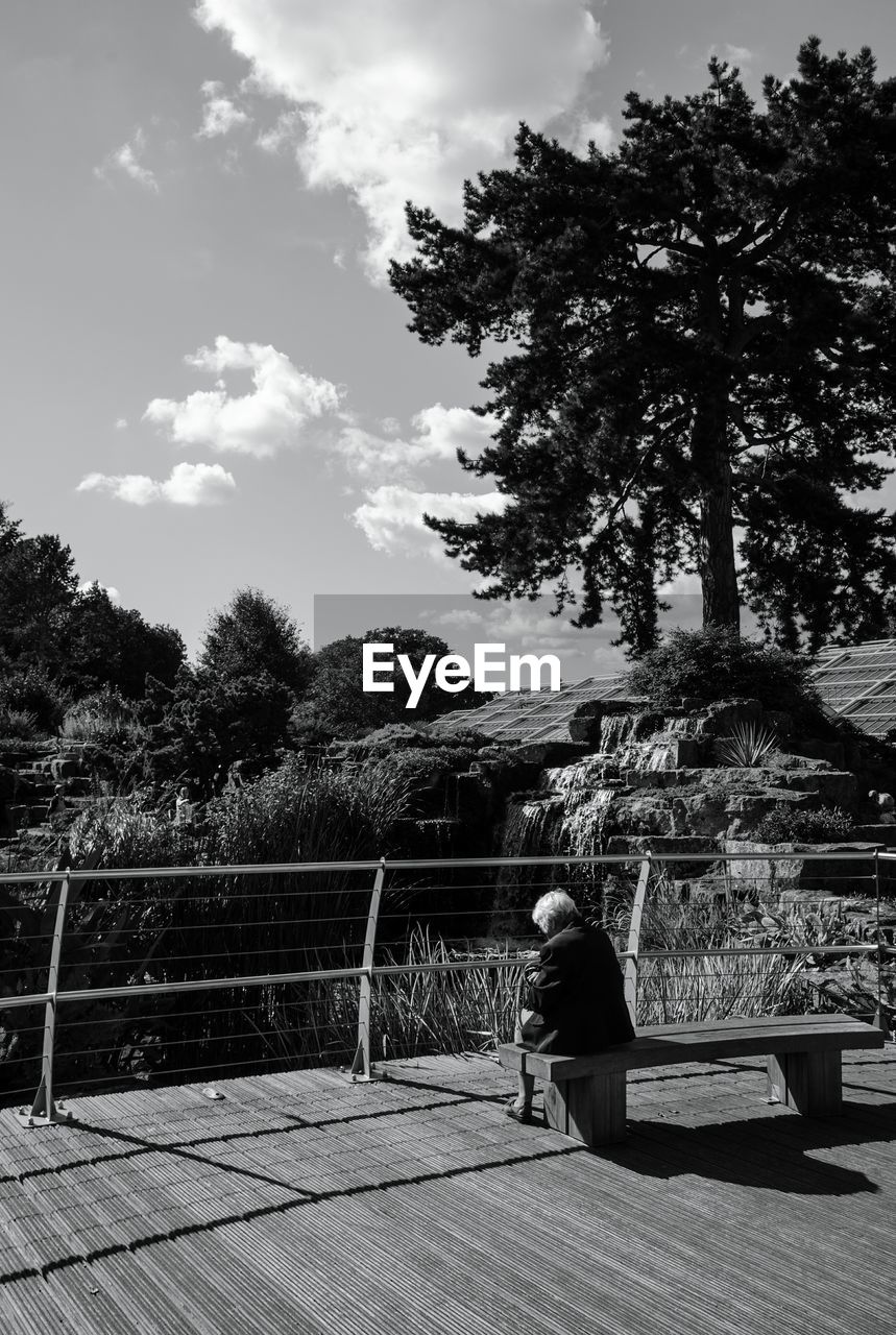 Rear view of person sitting on bench against sky