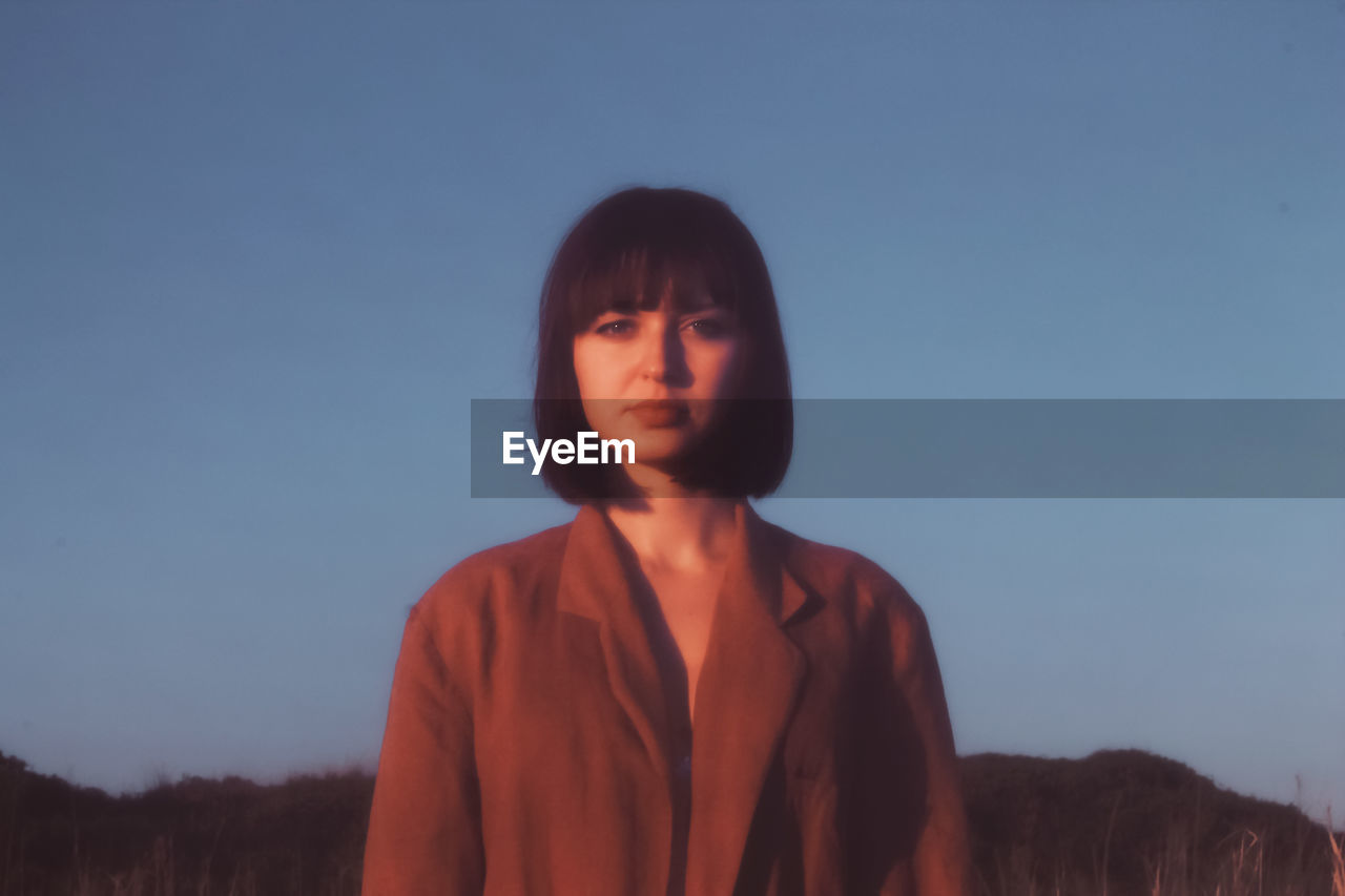 Portrait of young woman standing against clear sky during sunset