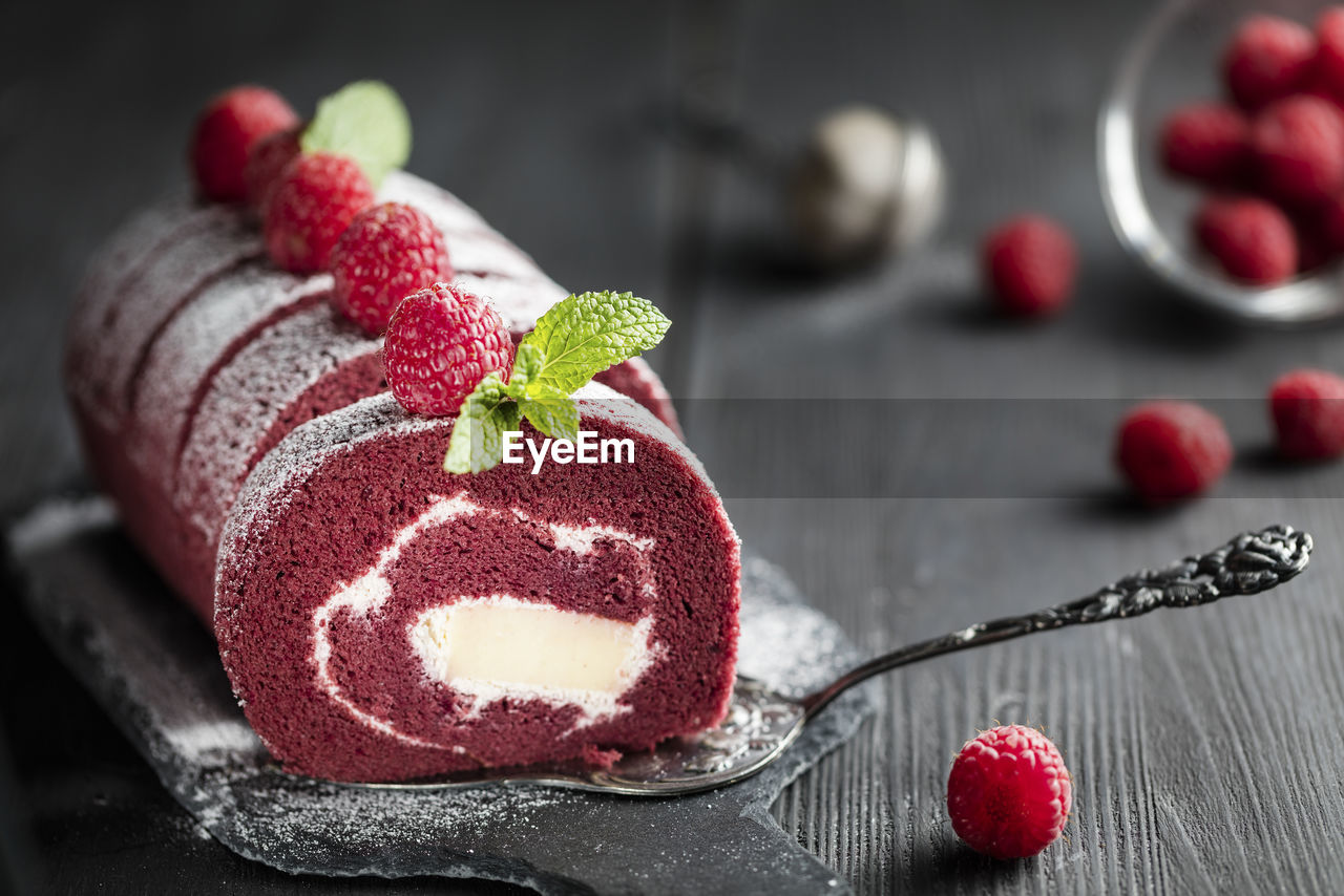 Red velvet sponge swiss roll with fresh raspberry and sugar icing on dark background