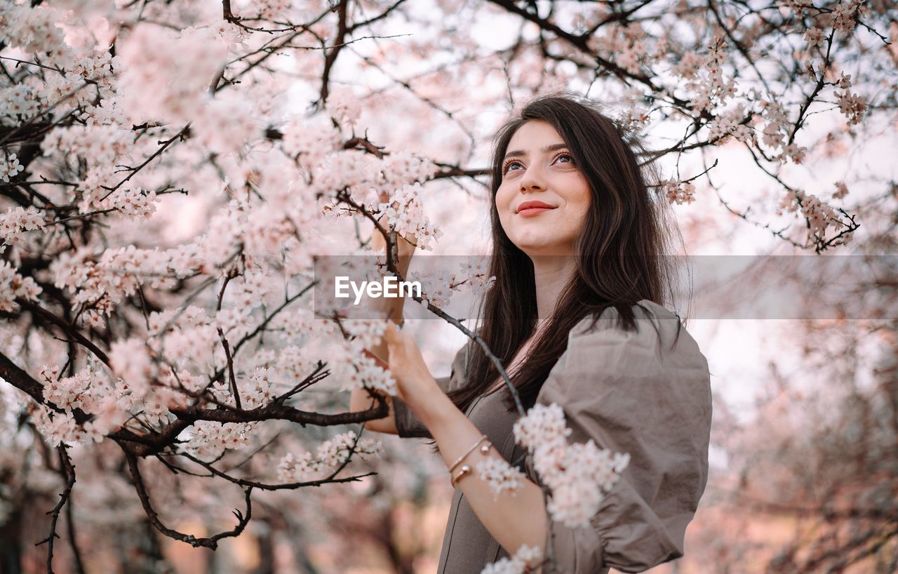 Beautiful young woman standing by cherry blossom tree