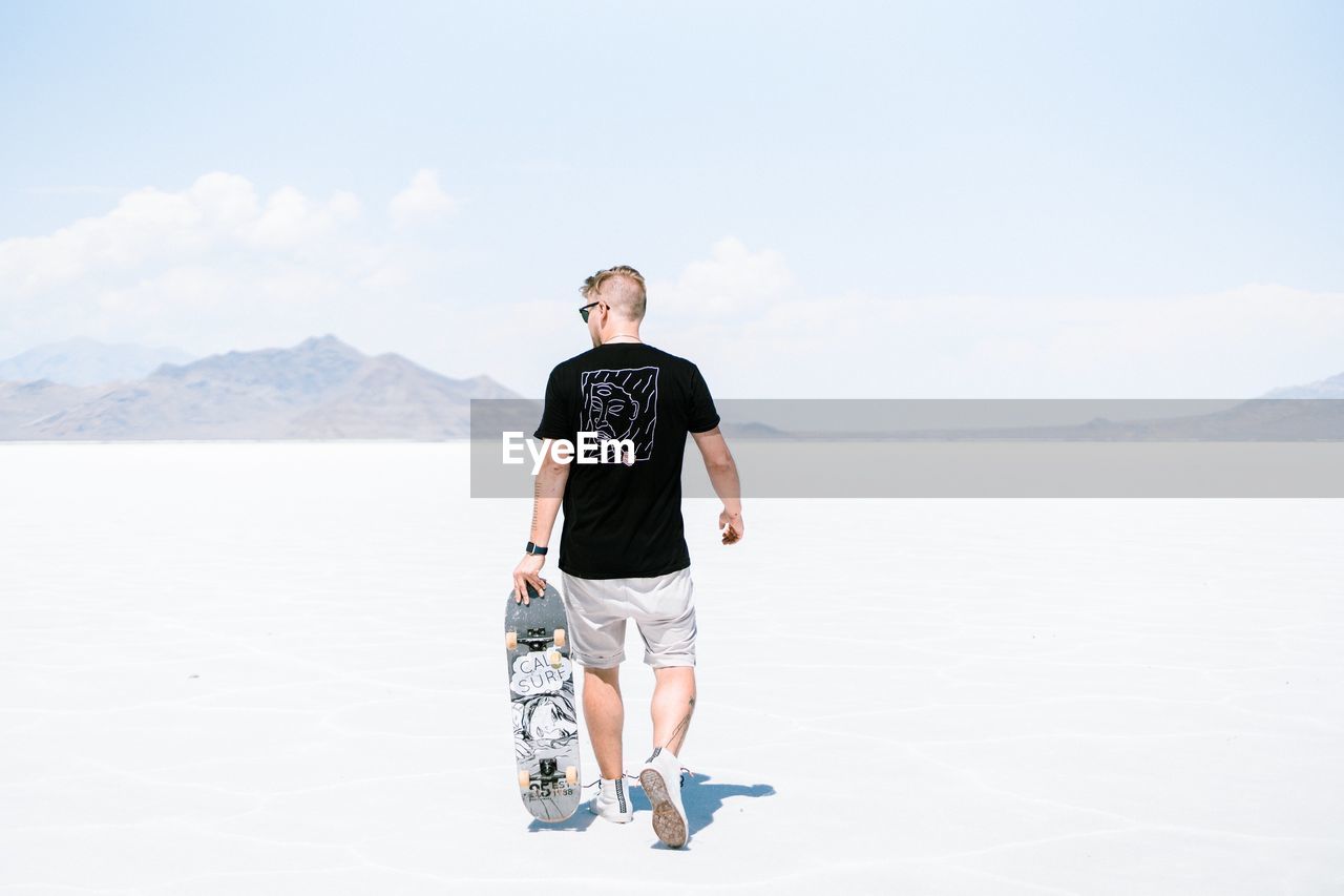 YOUNG MAN STANDING ON SHORE AGAINST SKY