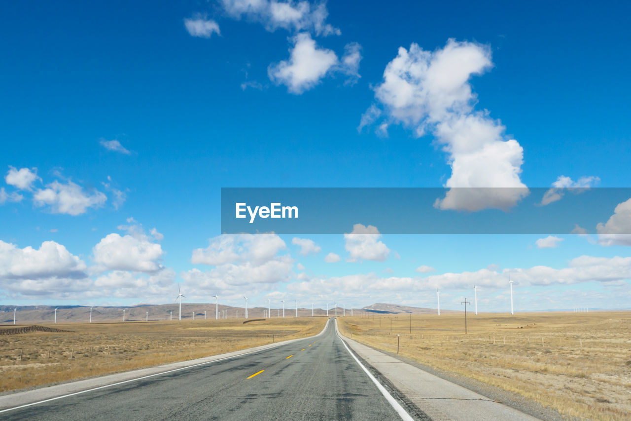 Empty road amidst land against blue sky