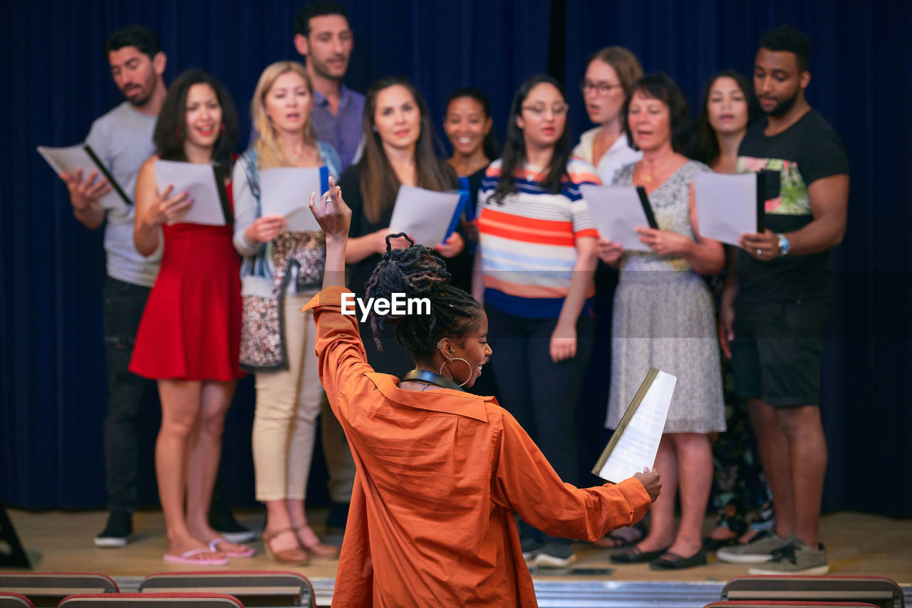 Young female conductor directing choir on stage in auditorium