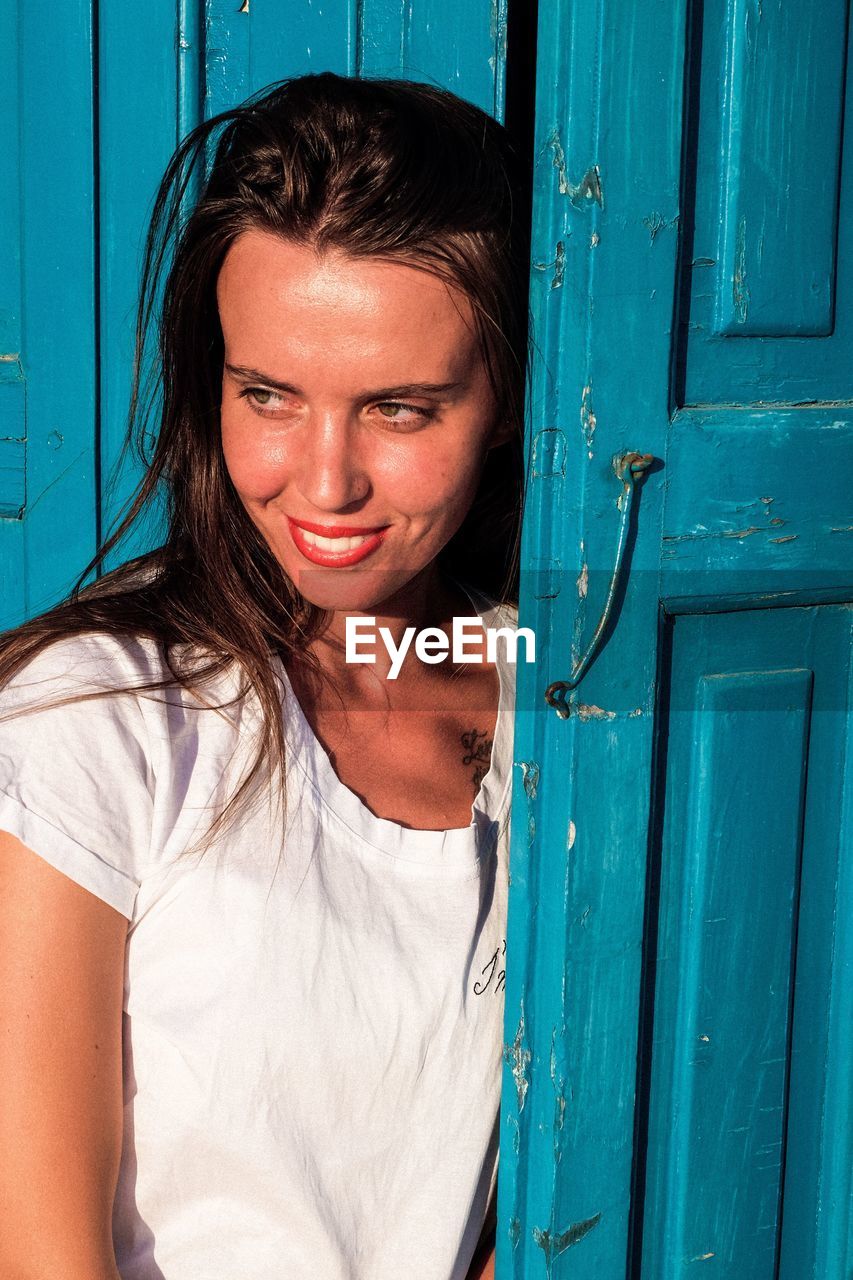 Young woman looking away while standing by blue door