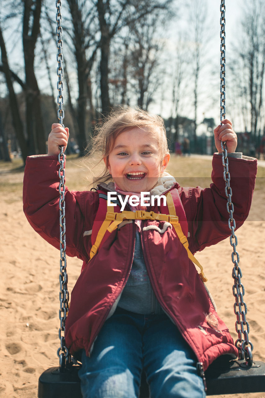 Portrait of smiling girl playing on swing at playground