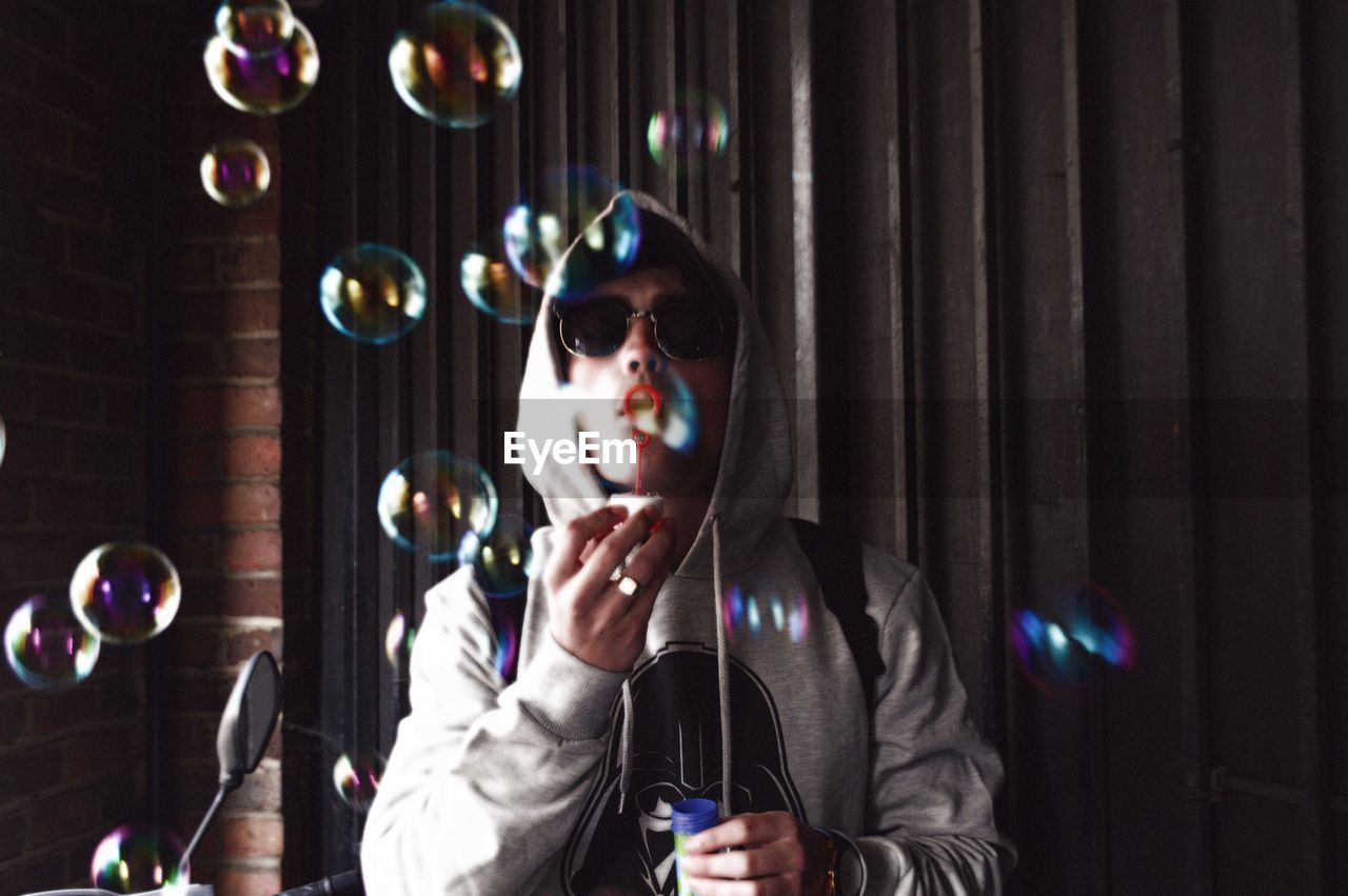 Man blowing bubbles while standing against wall