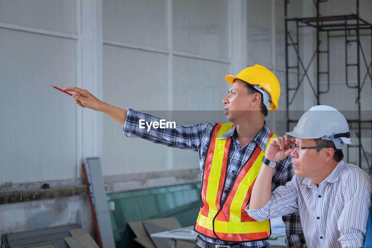 Architect pointing while explaining coworker at construction site