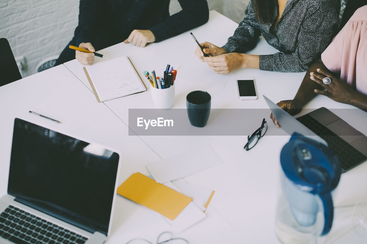 Midsection of creative business people sitting at conference table in board room