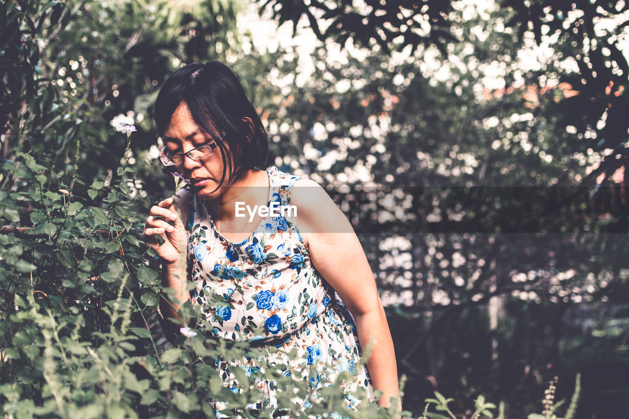 Woman smelling while standing by flowering plants