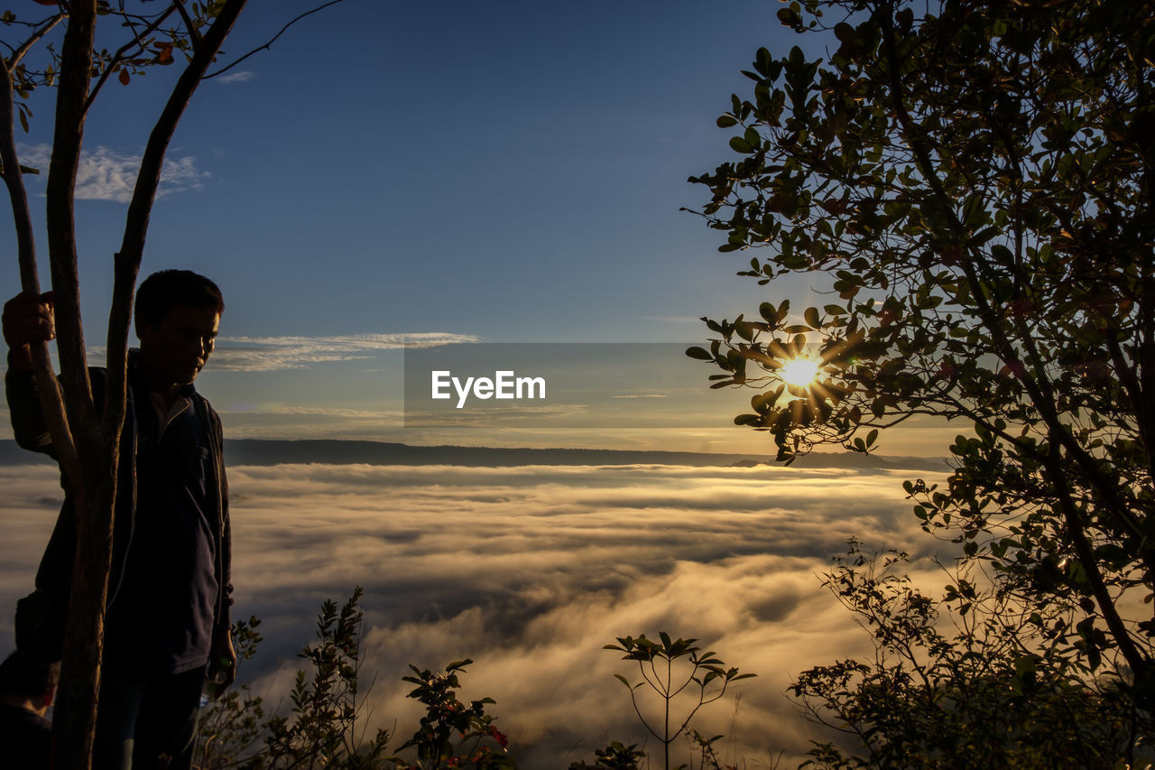 A male traveler exploring foggy top of mountain and looking at sunrise over mae khong river