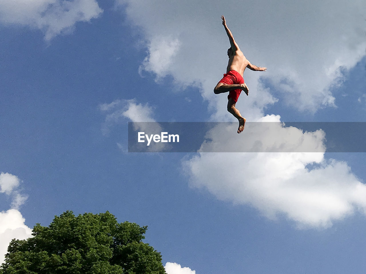 Low angle view of shirtless man in mid-air against sky