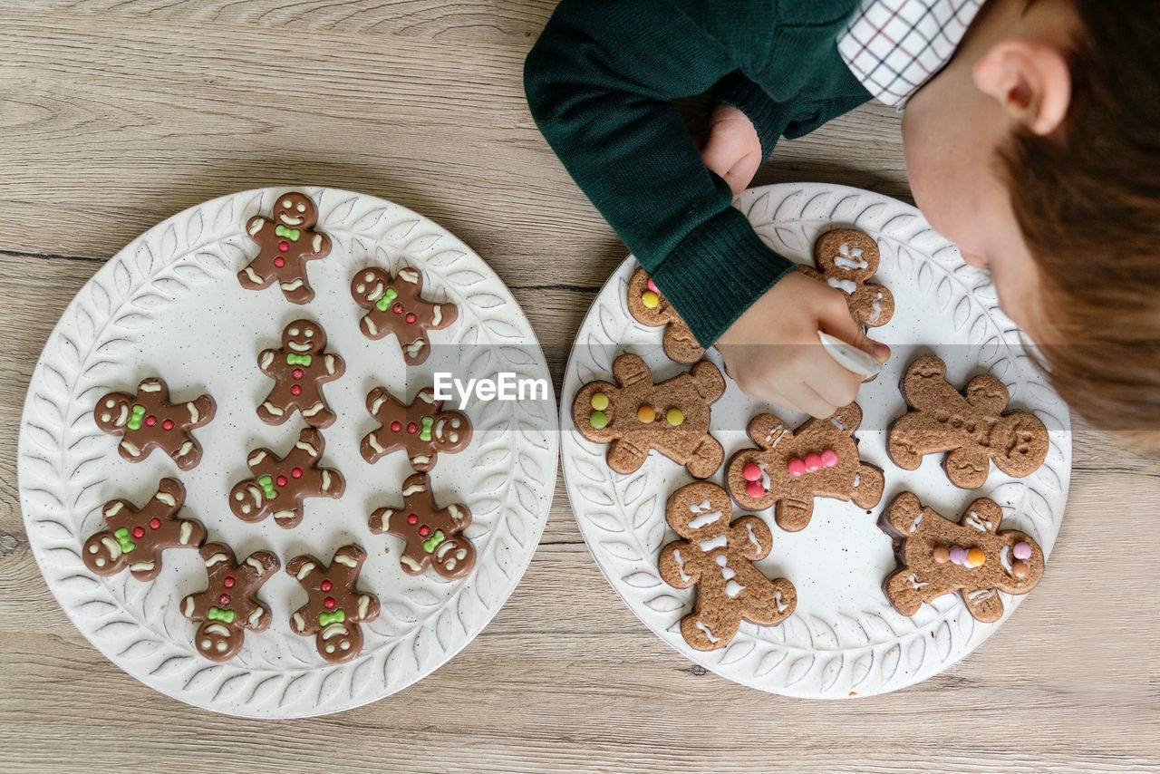 Cute boy decorating gingerbread cookies at home