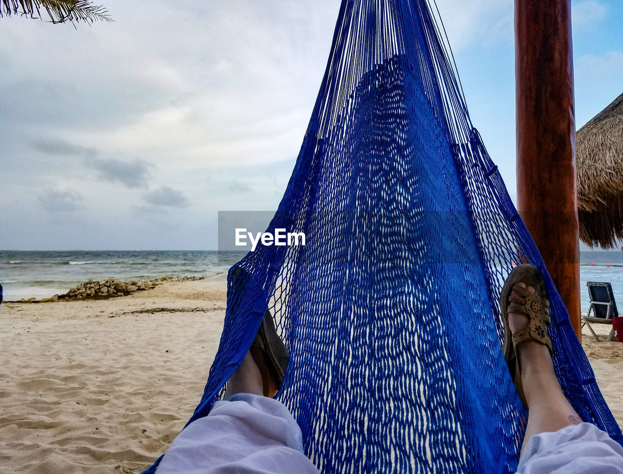 Low section of woman relaxing on hammock at beach against sky