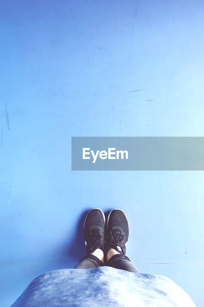 Low section of young woman wearing black shoes while standing on blue floor