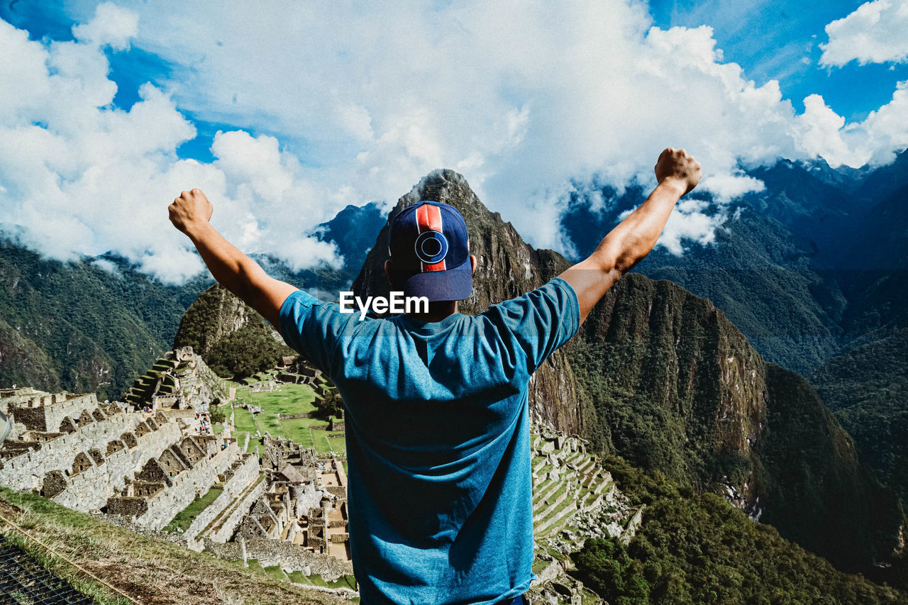 REAR VIEW OF MAN STANDING ON MOUNTAIN