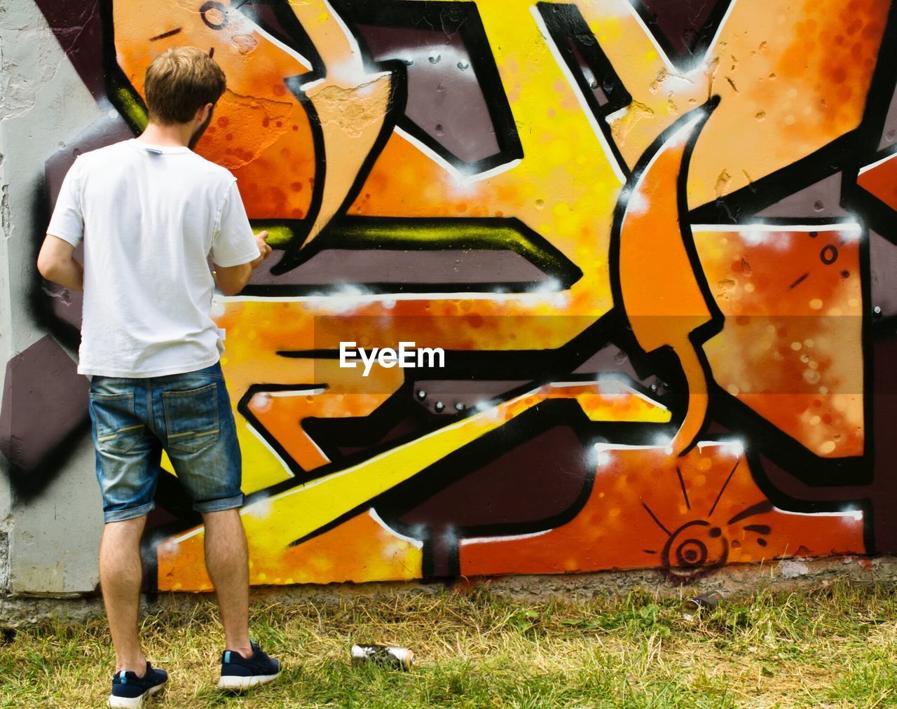 Street artist painting graffiti with aerosol can on wall
