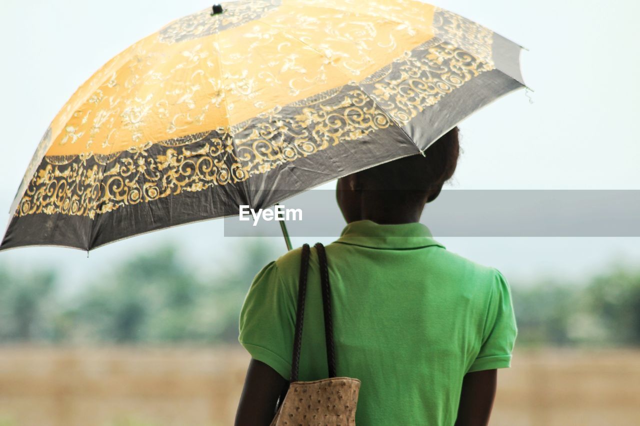 Rear view of woman with umbrella standing against sky