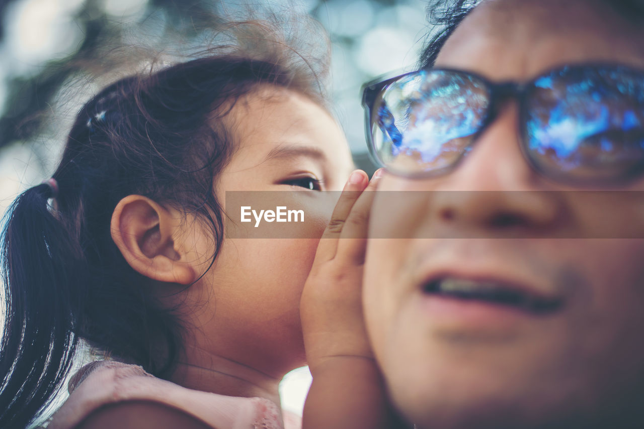 Close-up of daughter whispering in ear of father