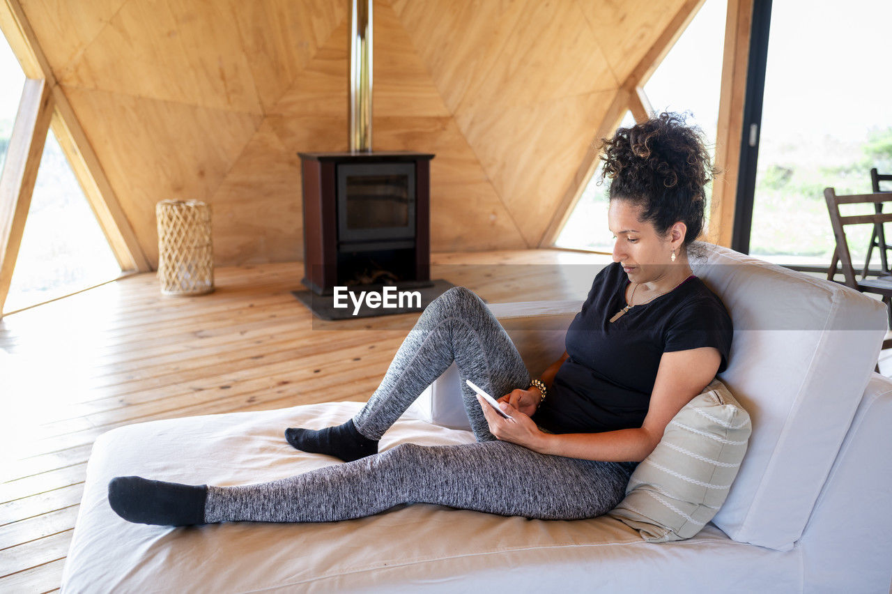 Woman using e reader while relaxing in a wooden dome tent.