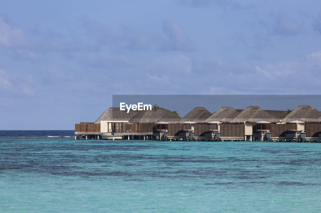 STILT HOUSES ON SEA BY BUILDINGS AGAINST SKY