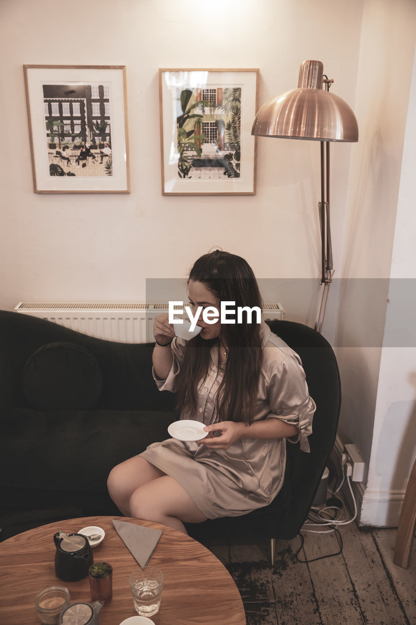 YOUNG WOMAN DRINKING GLASS WHILE SITTING ON TABLE