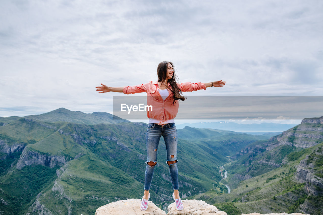 Beautiful woman with arms outstretched standing on cliff against mountain