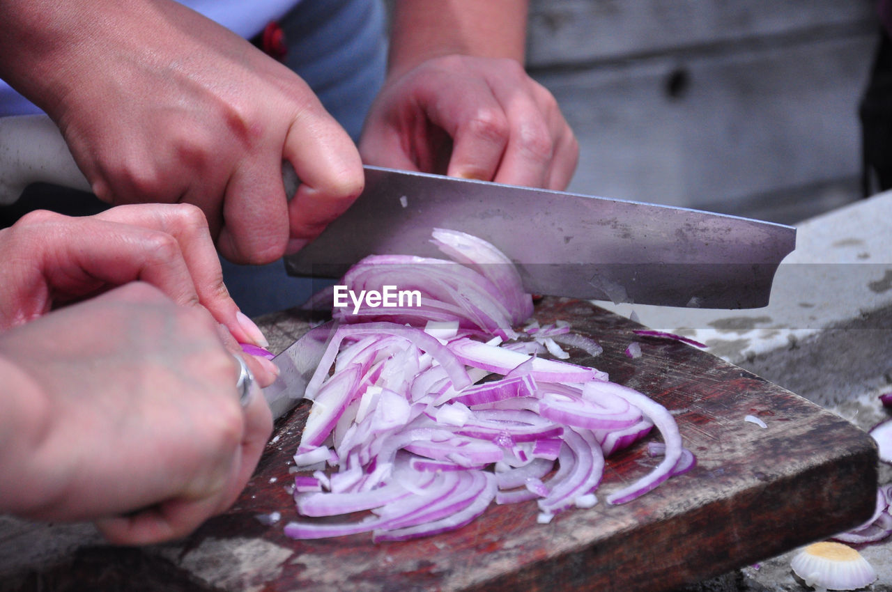 Cropped image of man and woman chopping onions in kitchen