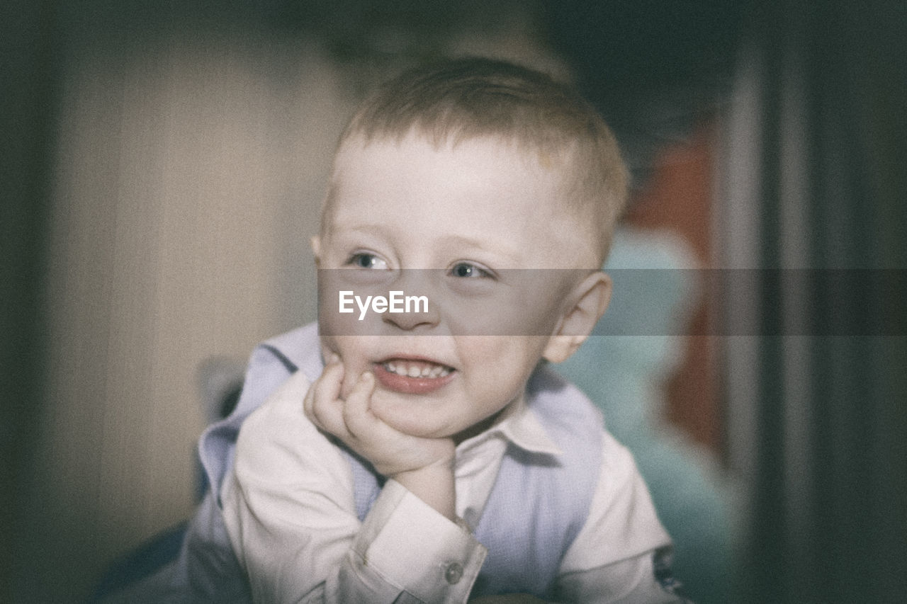 Close-up of smiling boy with hand on chin at home