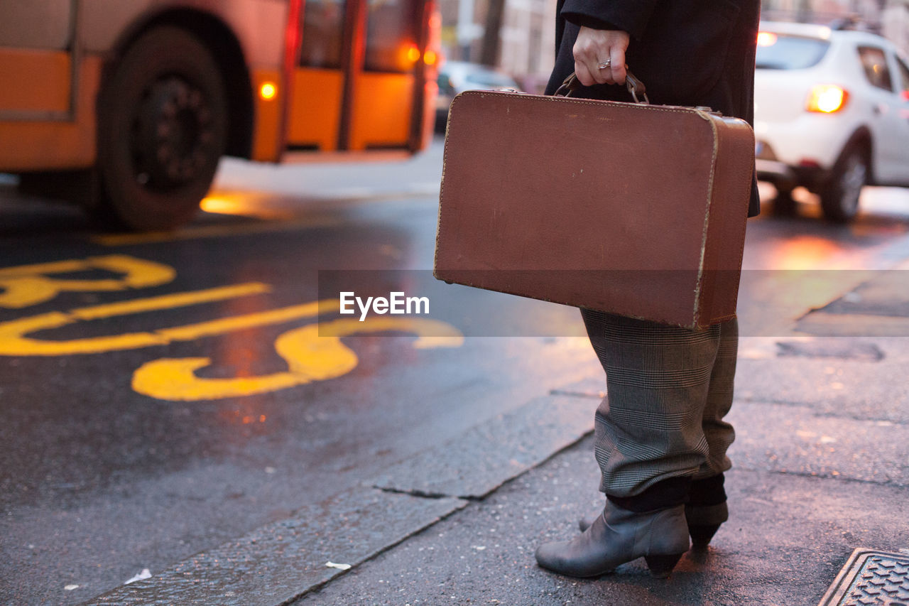 Low section of businessman carrying suitcase while standing on city street