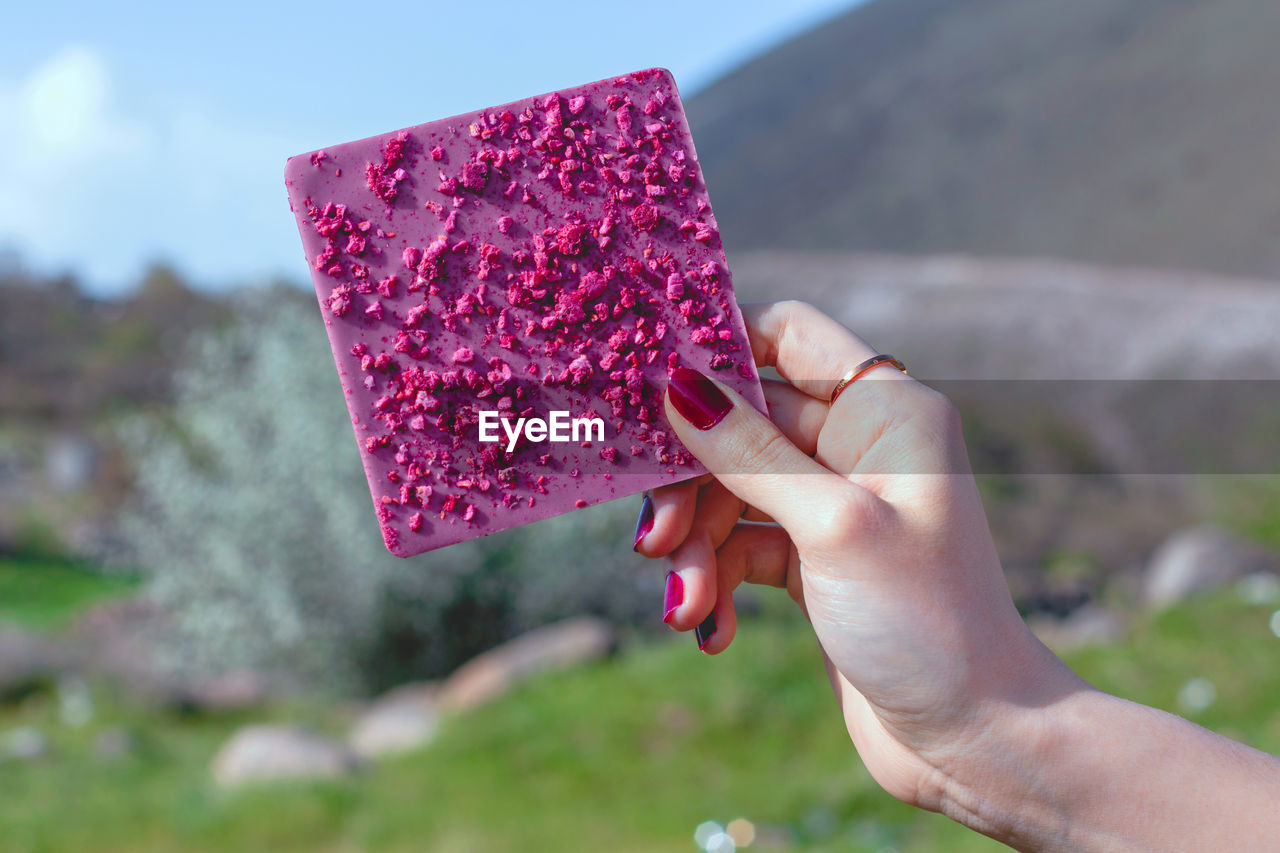 CLOSE-UP OF HAND HOLDING RED CAKE