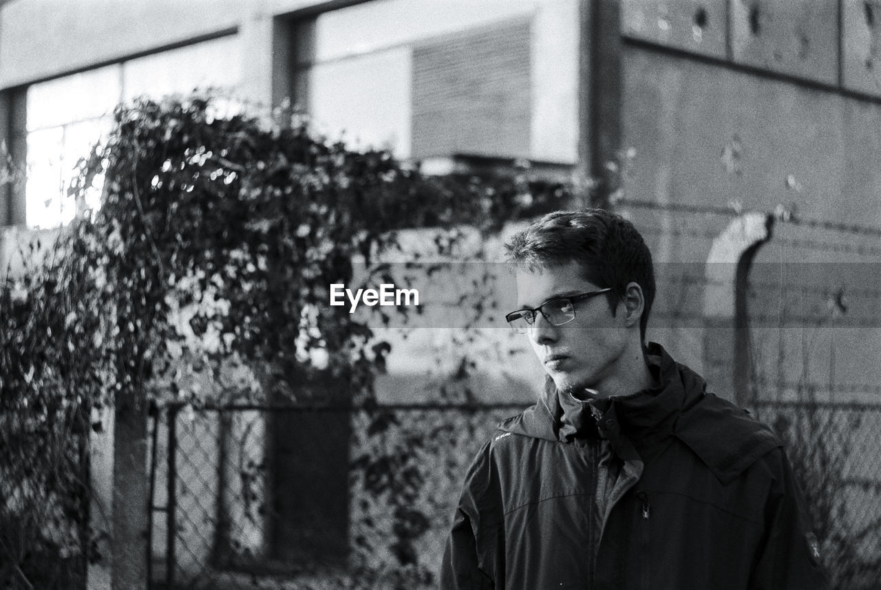 Young man wearing eyeglasses looking away while standing against building