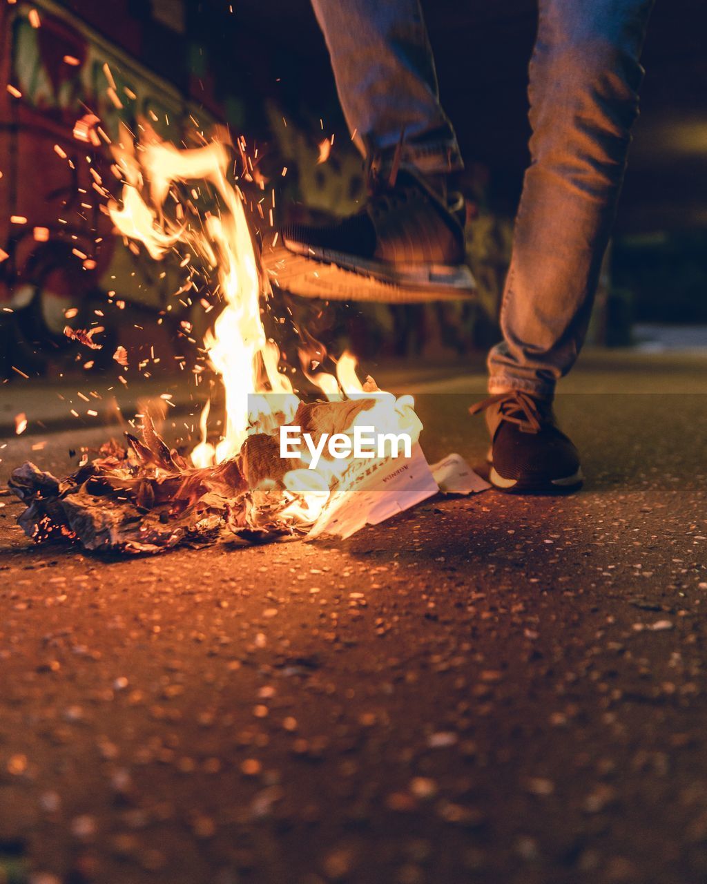 Low section of man standing by burning papers on street at night