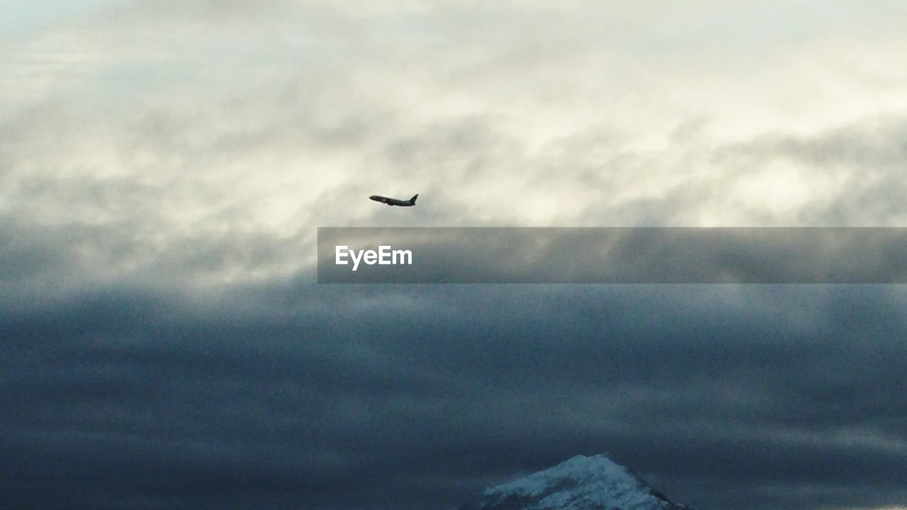 LOW ANGLE VIEW OF AIRPLANE FLYING OVER CLOUDY SKY