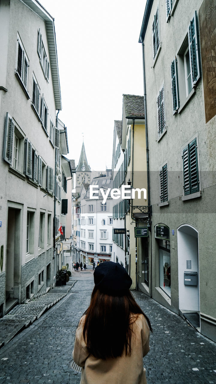 Rear view of woman standing on street amidst buildings in city