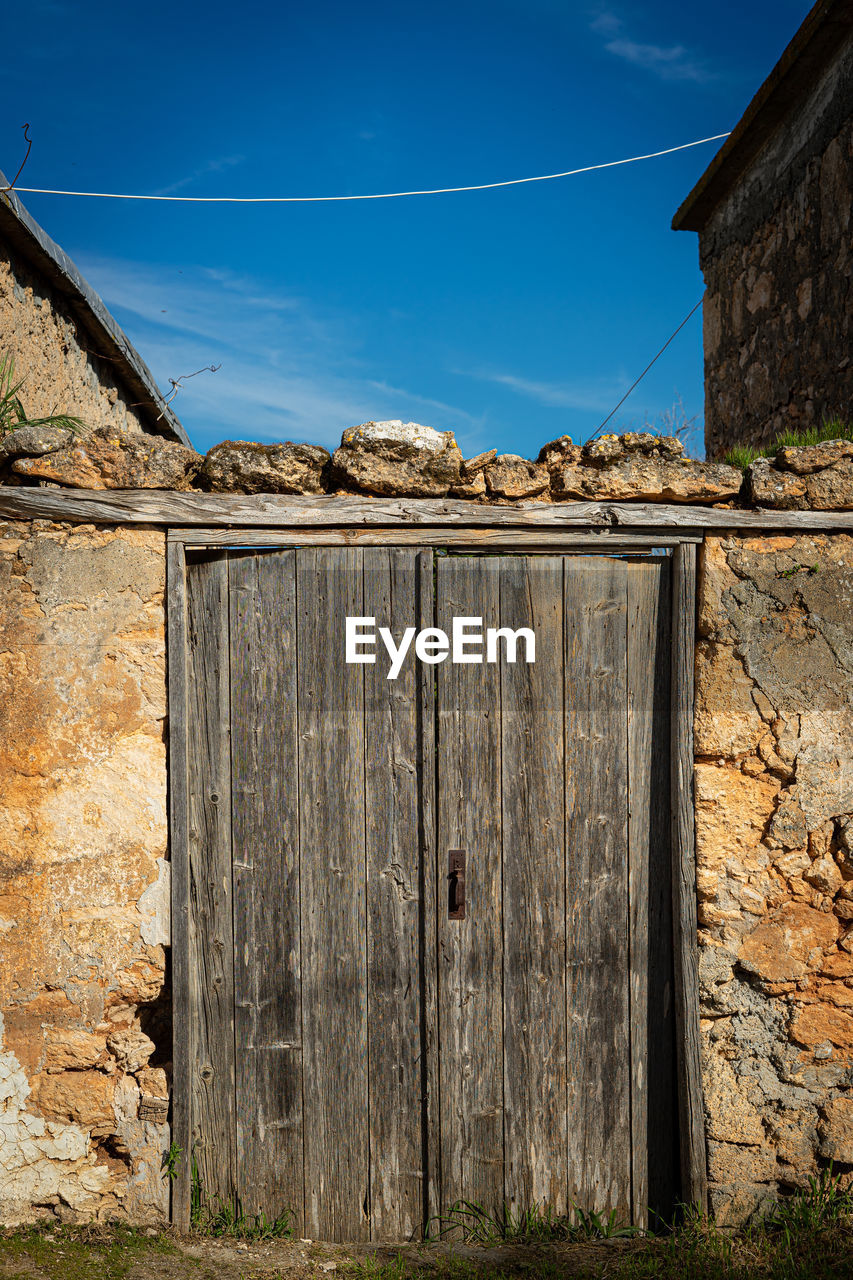 Abandoned building and old wooden door against blue sky