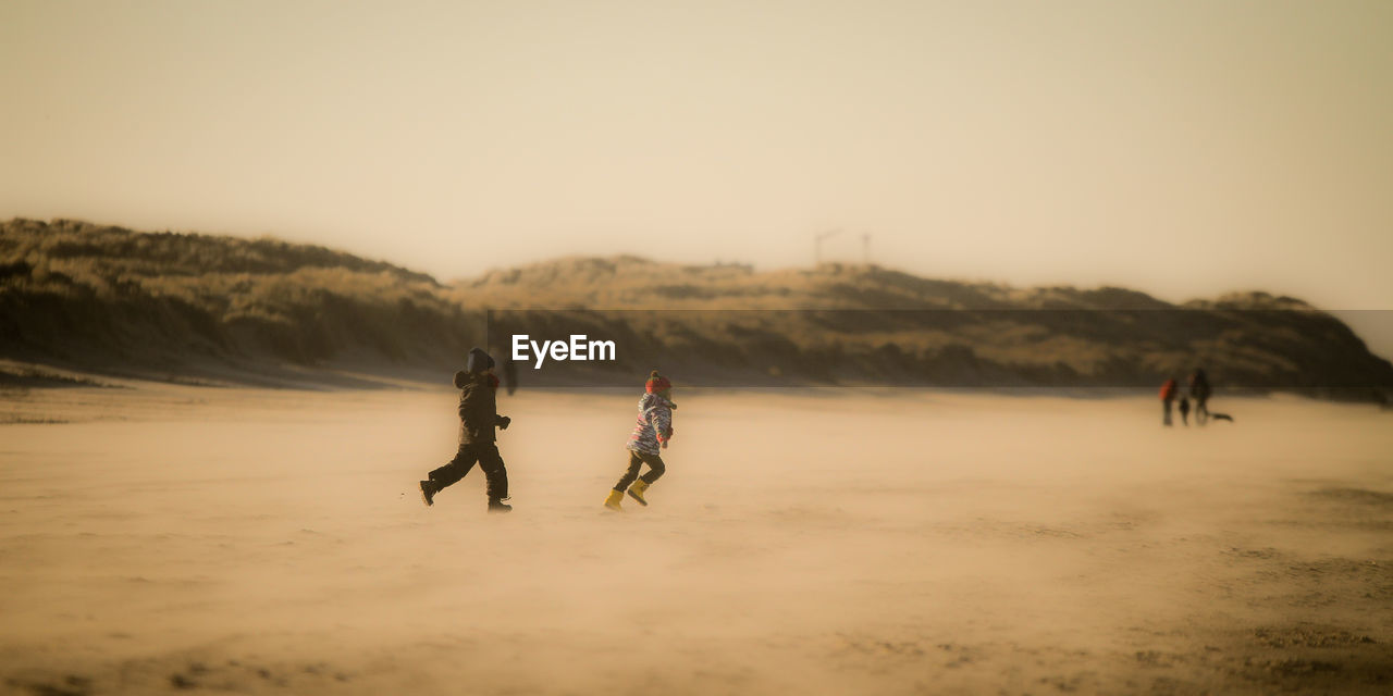 Boys running at beach against clear sky