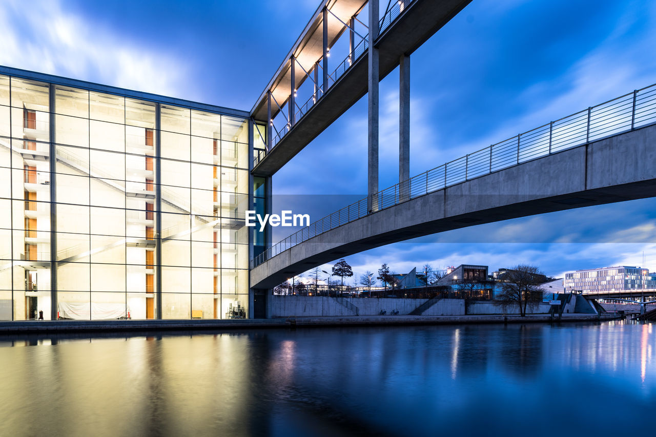 Bridge over river against sky in city at dusk